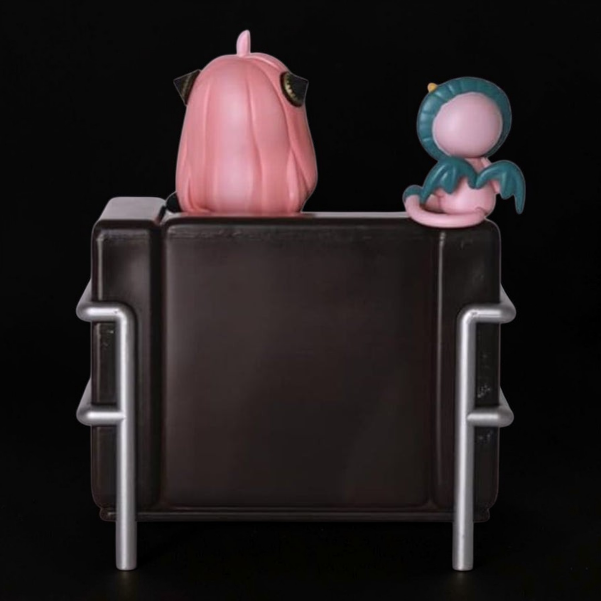Two pink character figurines sitting on a black chair against a black background
