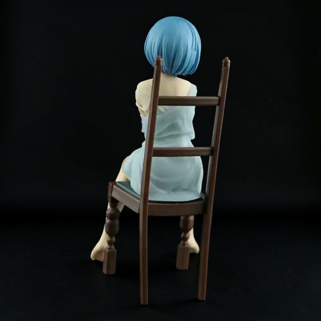 Anime character figurine sitting on a chair in a cozy room with a bookshelf and bed.