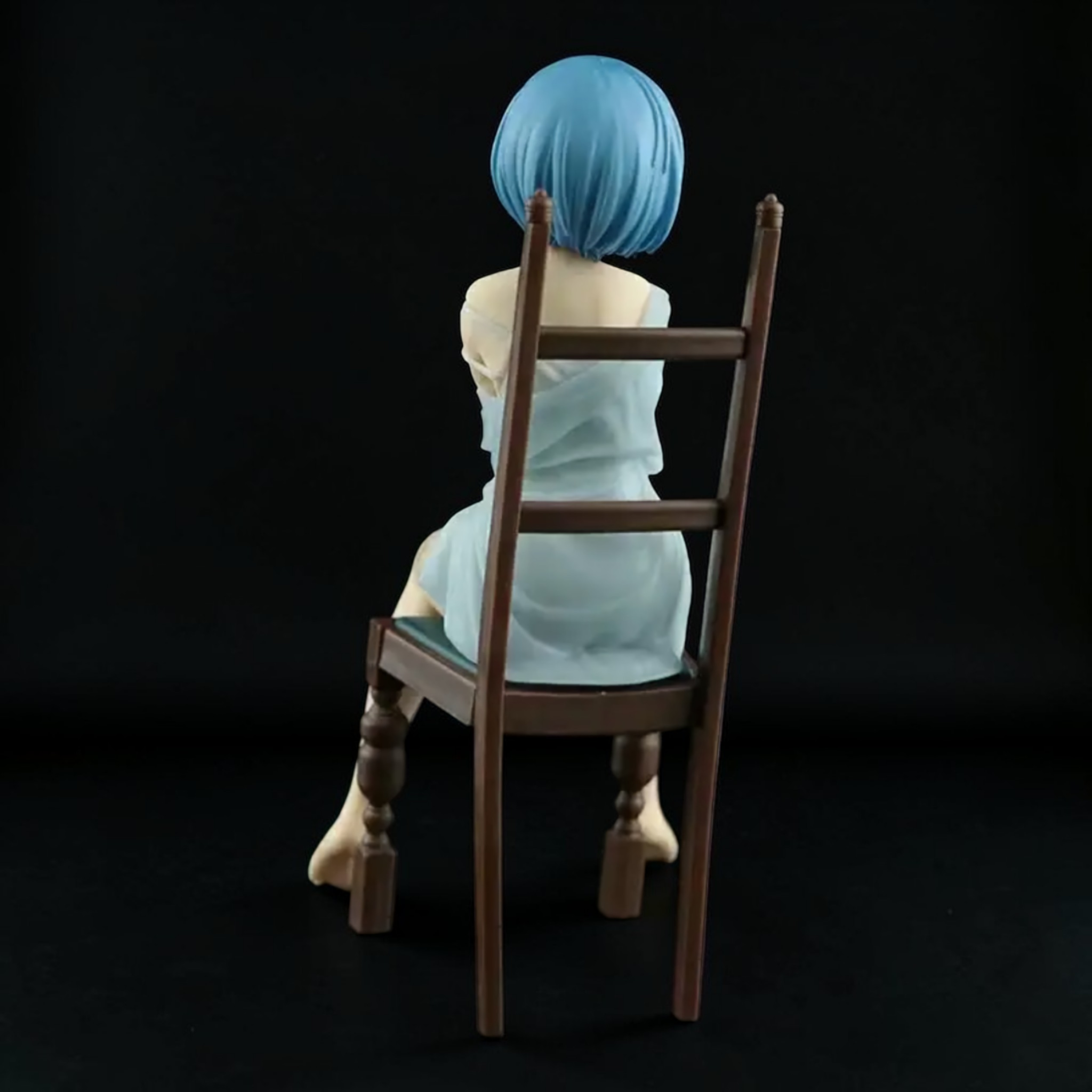 Figure with blue hair sitting on a wooden chair against a black background