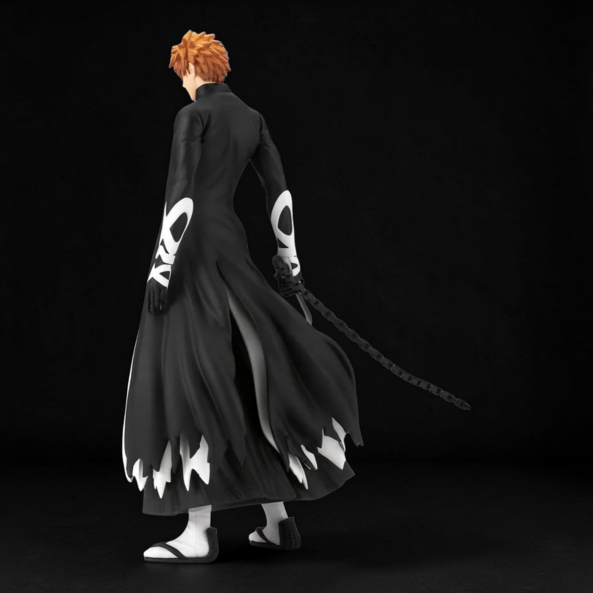 Figure of a character in a black outfit with white designs, holding a sword on a black background