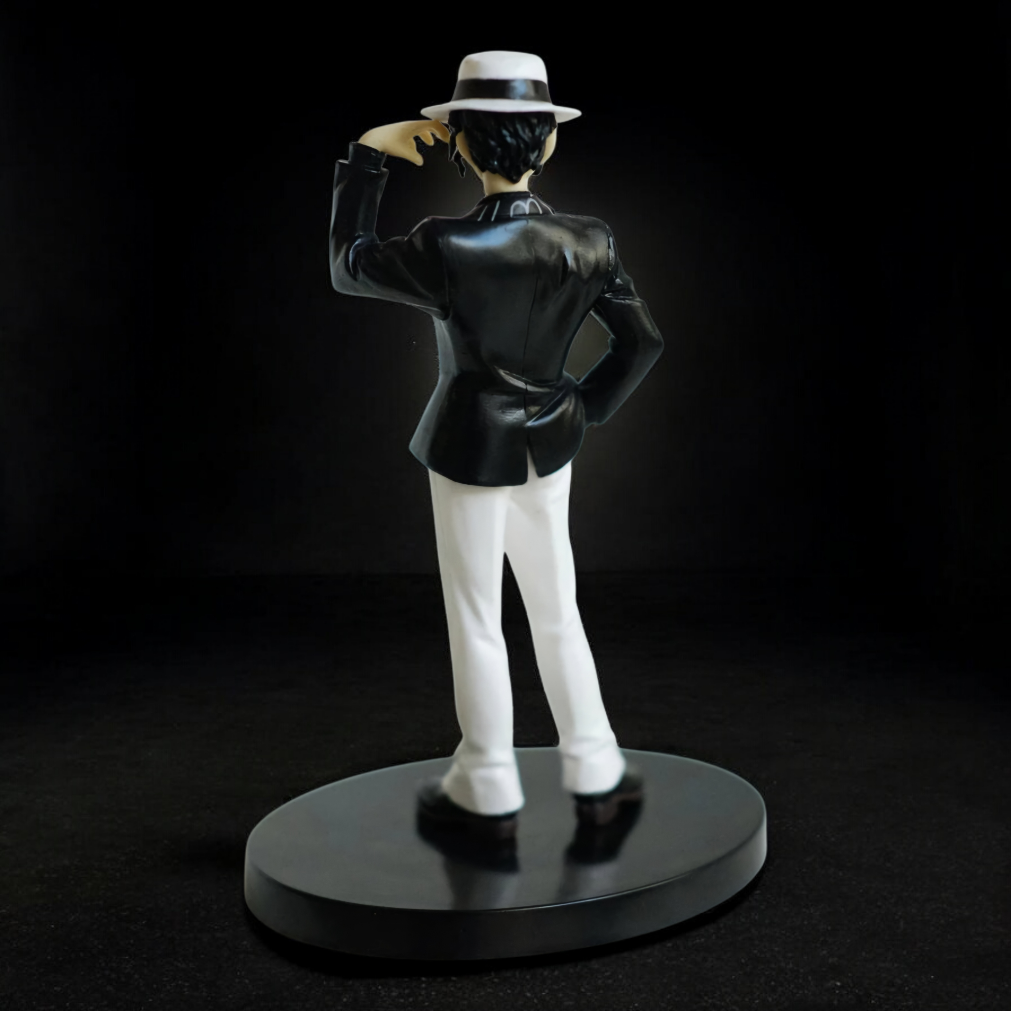 Statue of a person in a black suit and hat on a black background