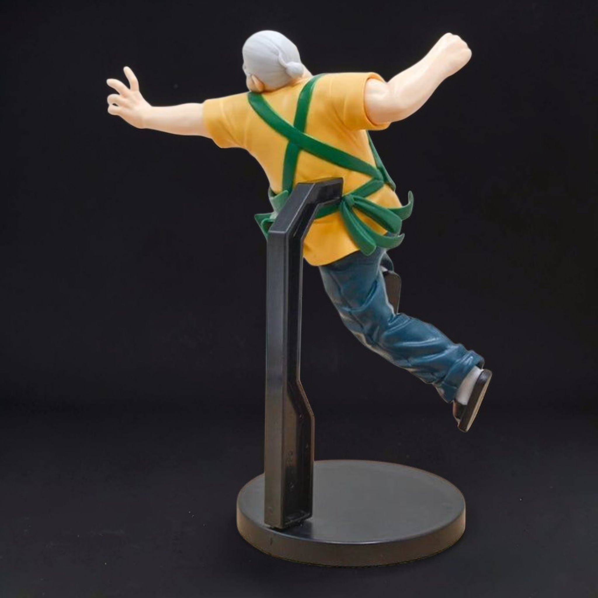 Figurine of a person in yellow shirt and green harness on a black stand against a black background