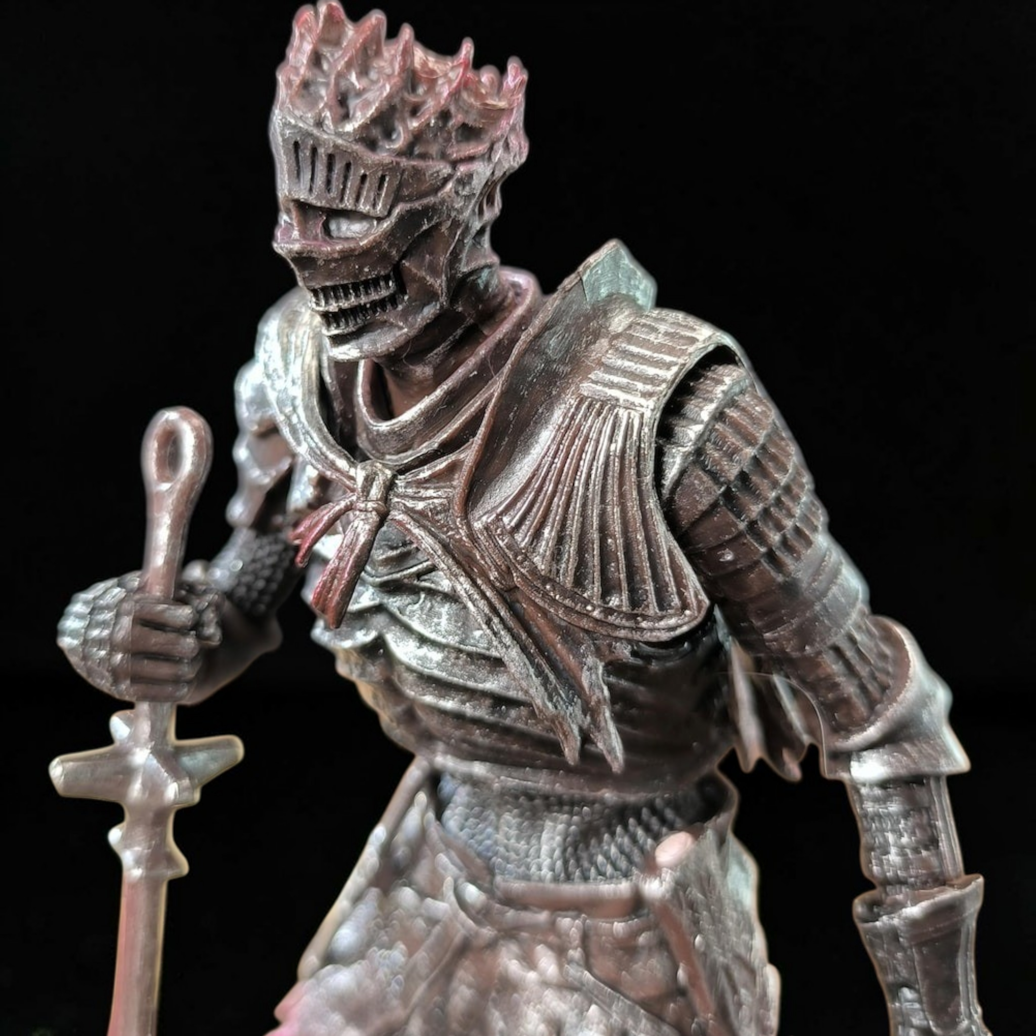 Metallic figurine of a warrior holding a staff against a black background