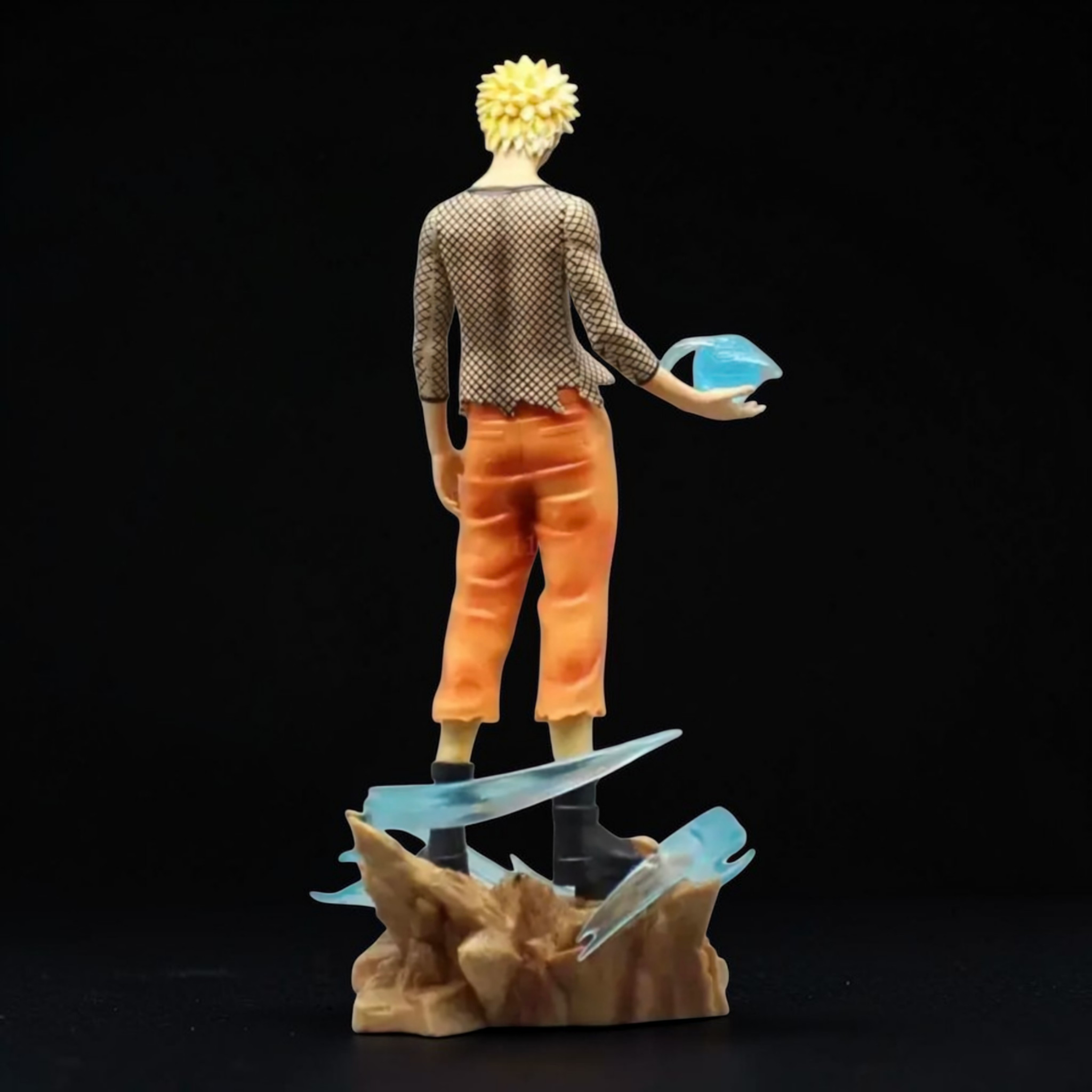 Figurine of a character with spiky hair, wearing an orange outfit and holding a blue object, on a dark background.