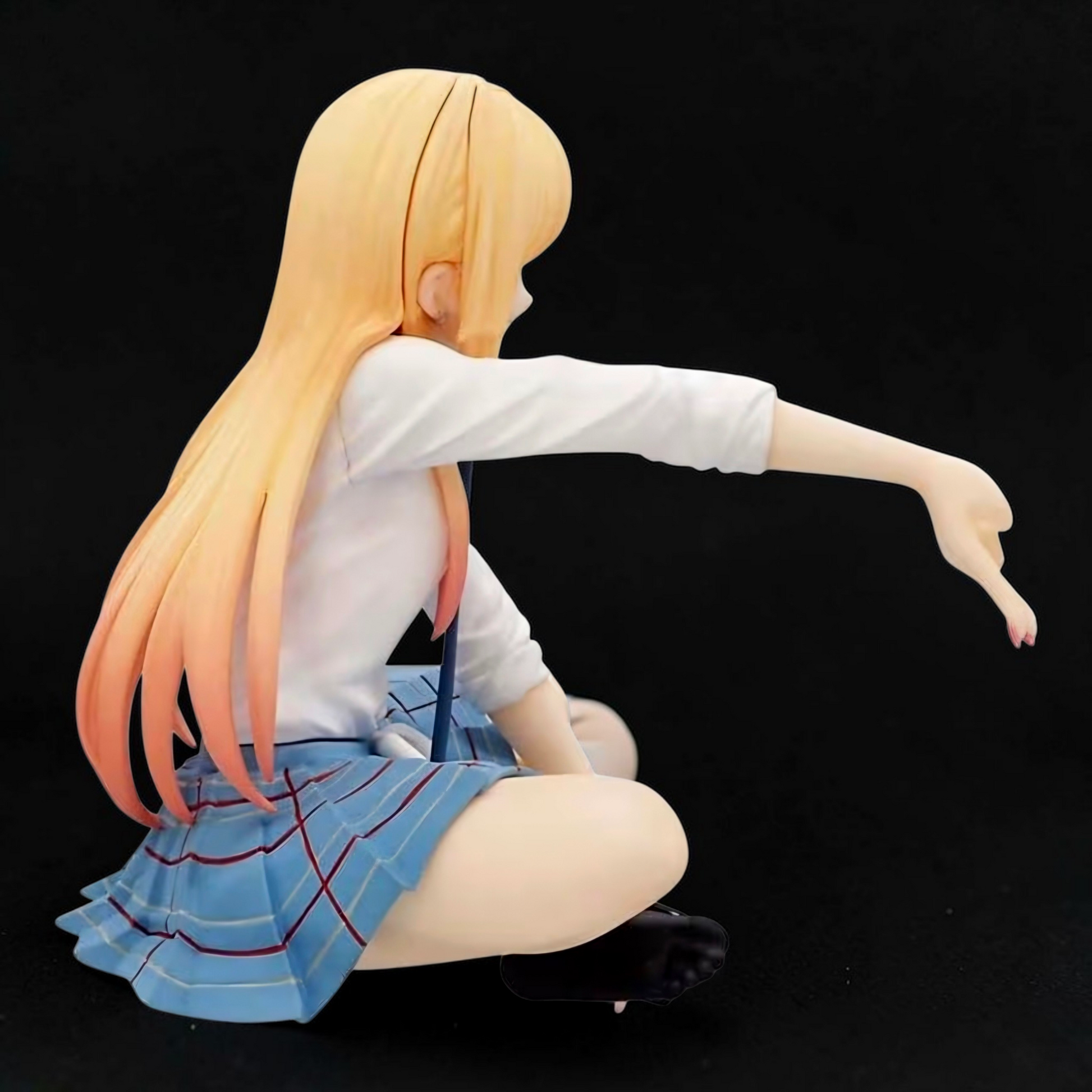 Figurine of a character with long hair, wearing a white shirt and blue skirt, sitting on a black background.