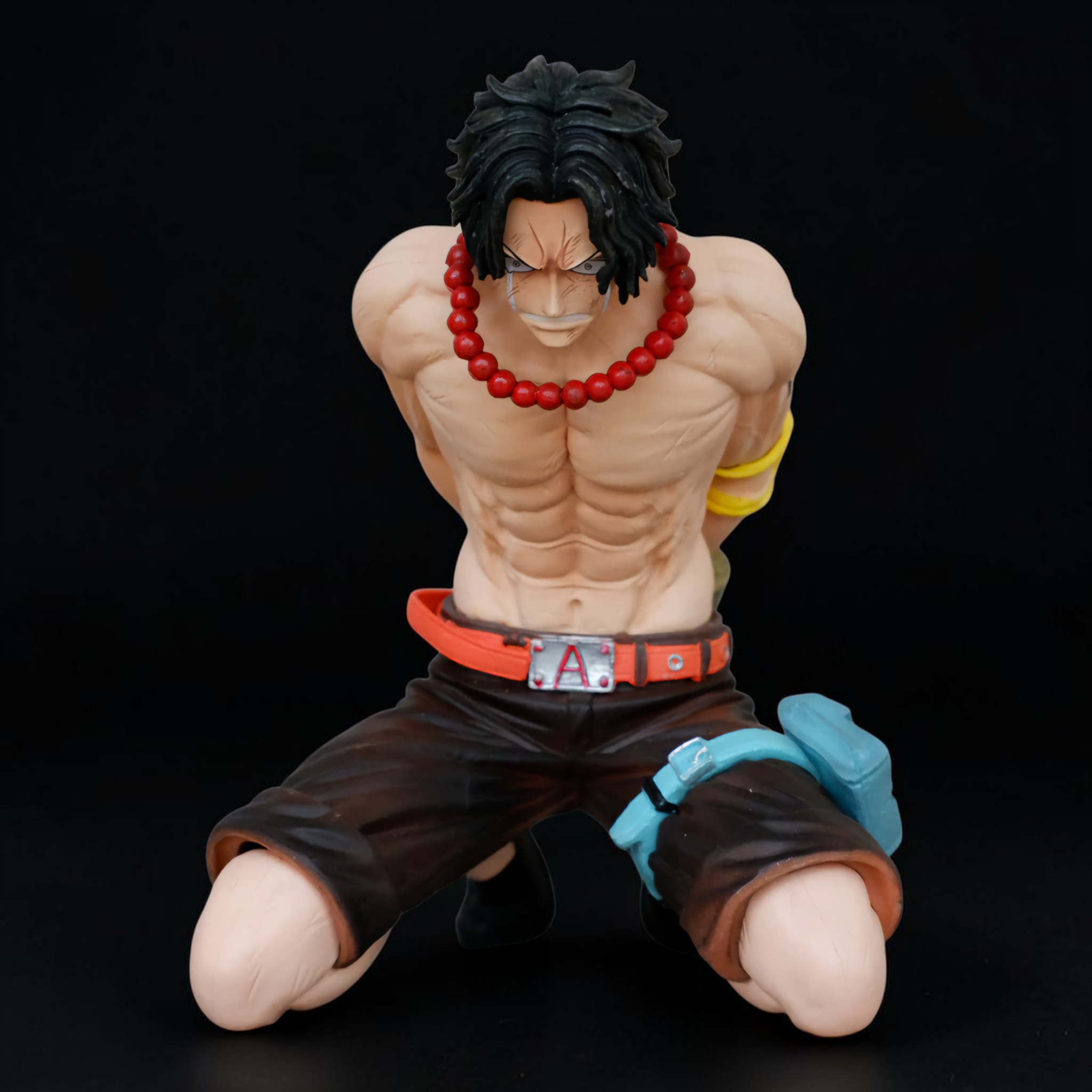 Action figure of a muscular character with a red necklace and black hair on a black background